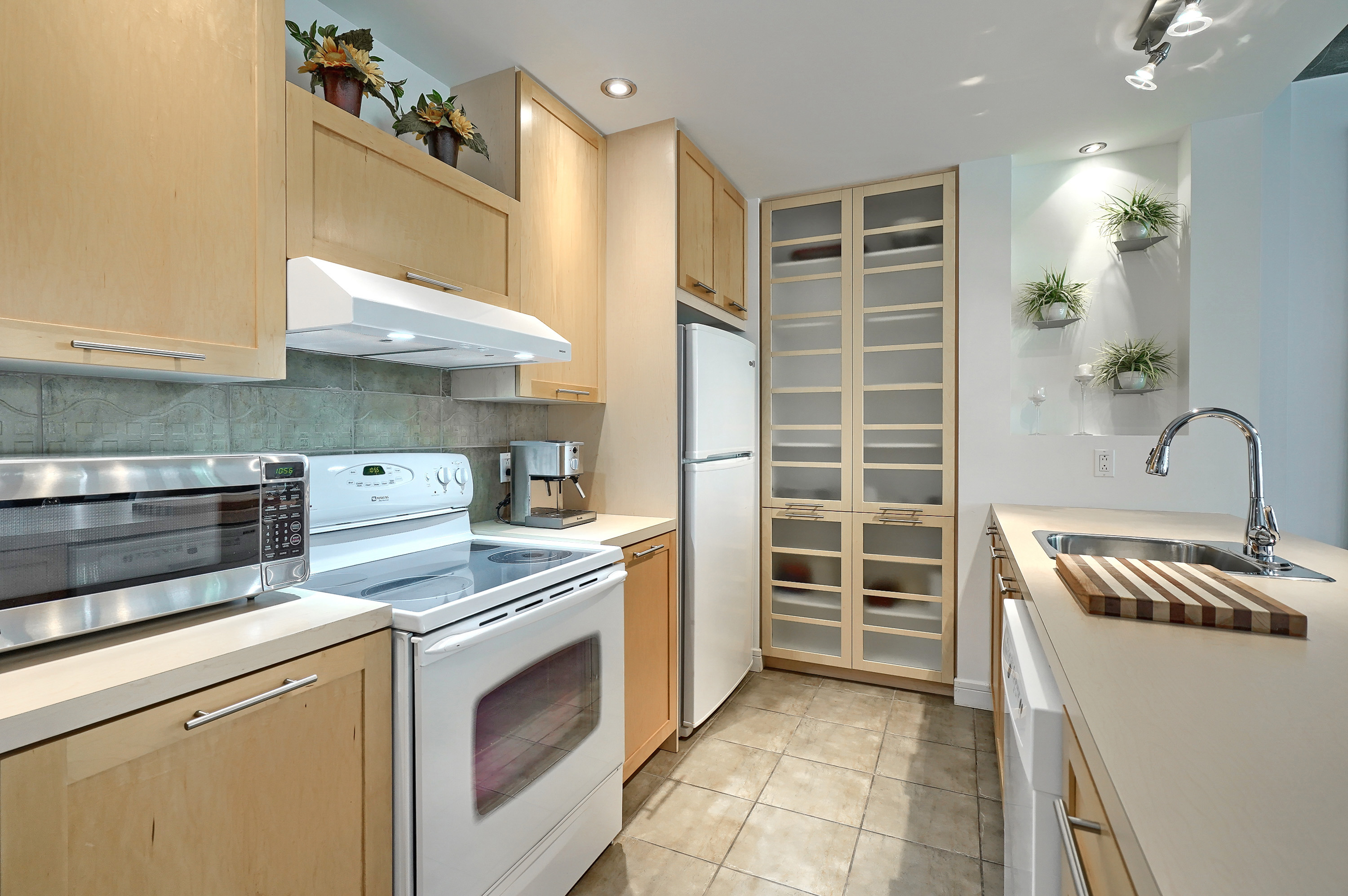 View of the kitchen area showing the appliances. There is plenty of storage in this modern kitchen in light wood and white. Another reason to choose this furnished apartment for rent Montreal