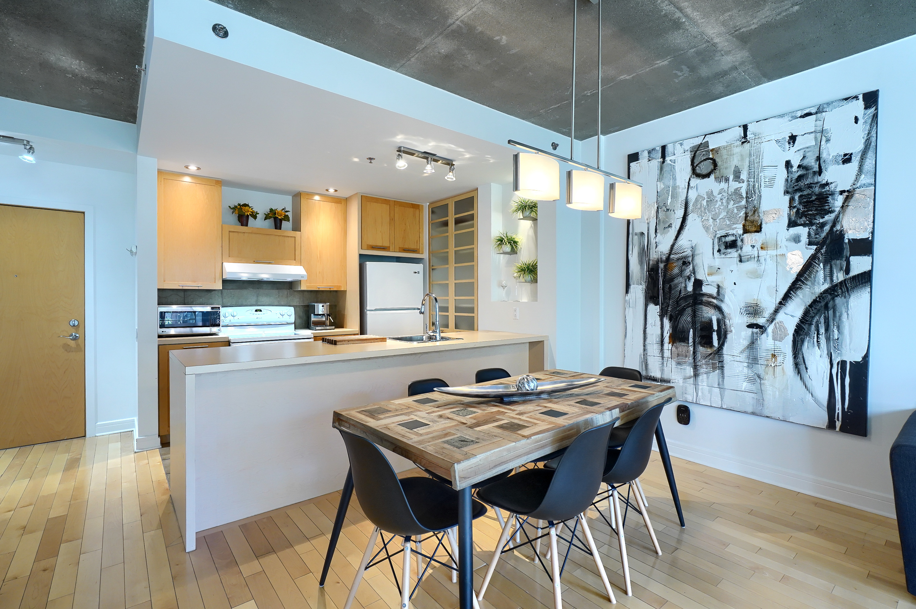 Angled view of the dinning area with a wood table with 6 chairs, giant painting on the wall and a peek of the completely equipped kitchen of this luxury furnished apartment for rent in Montreal