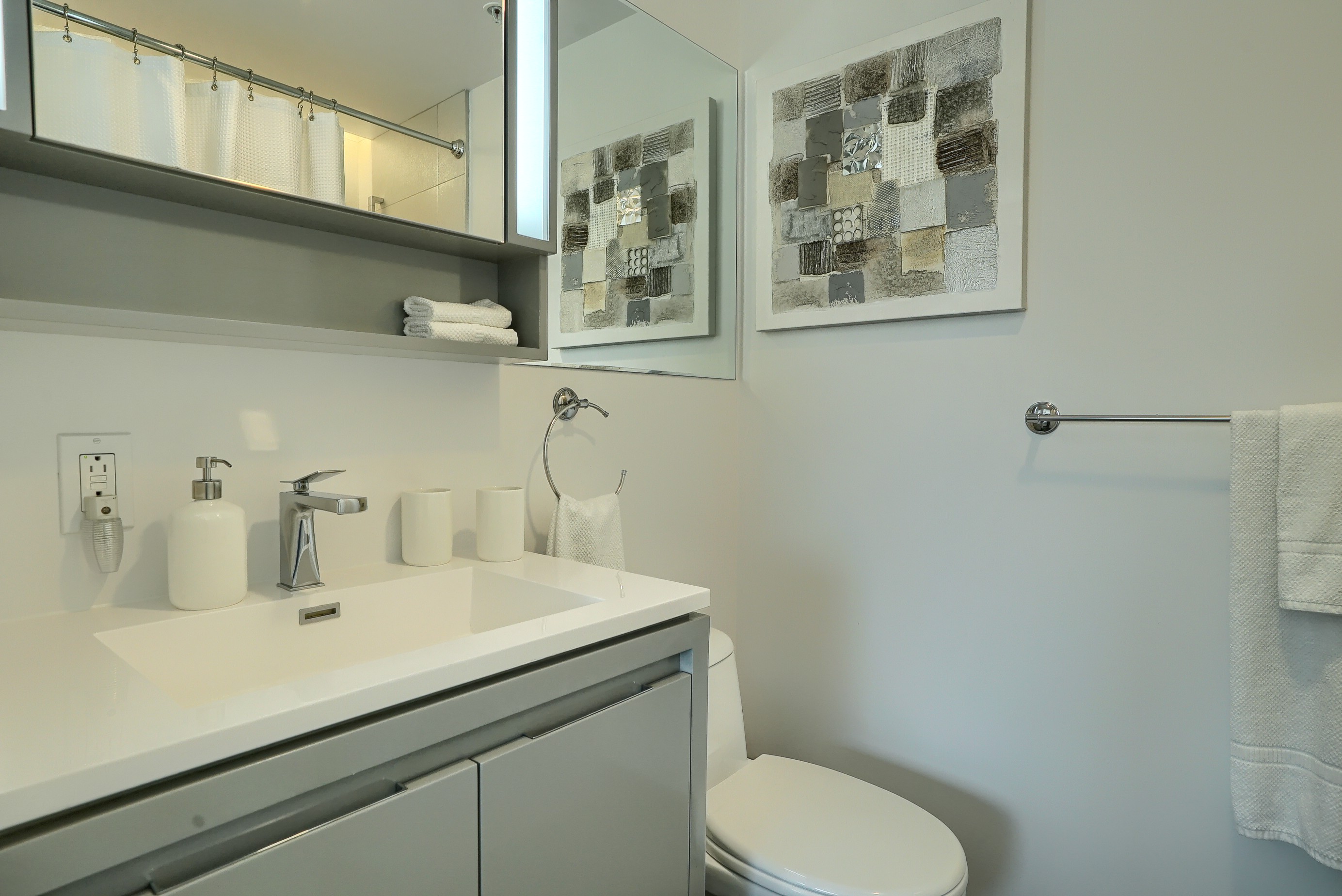 Vue en angle de la deuxième salle de bain de cet location corporative meublée à Montréal. Évier blanc surdimensionné avec robinet design et grand miroir bien éclairé