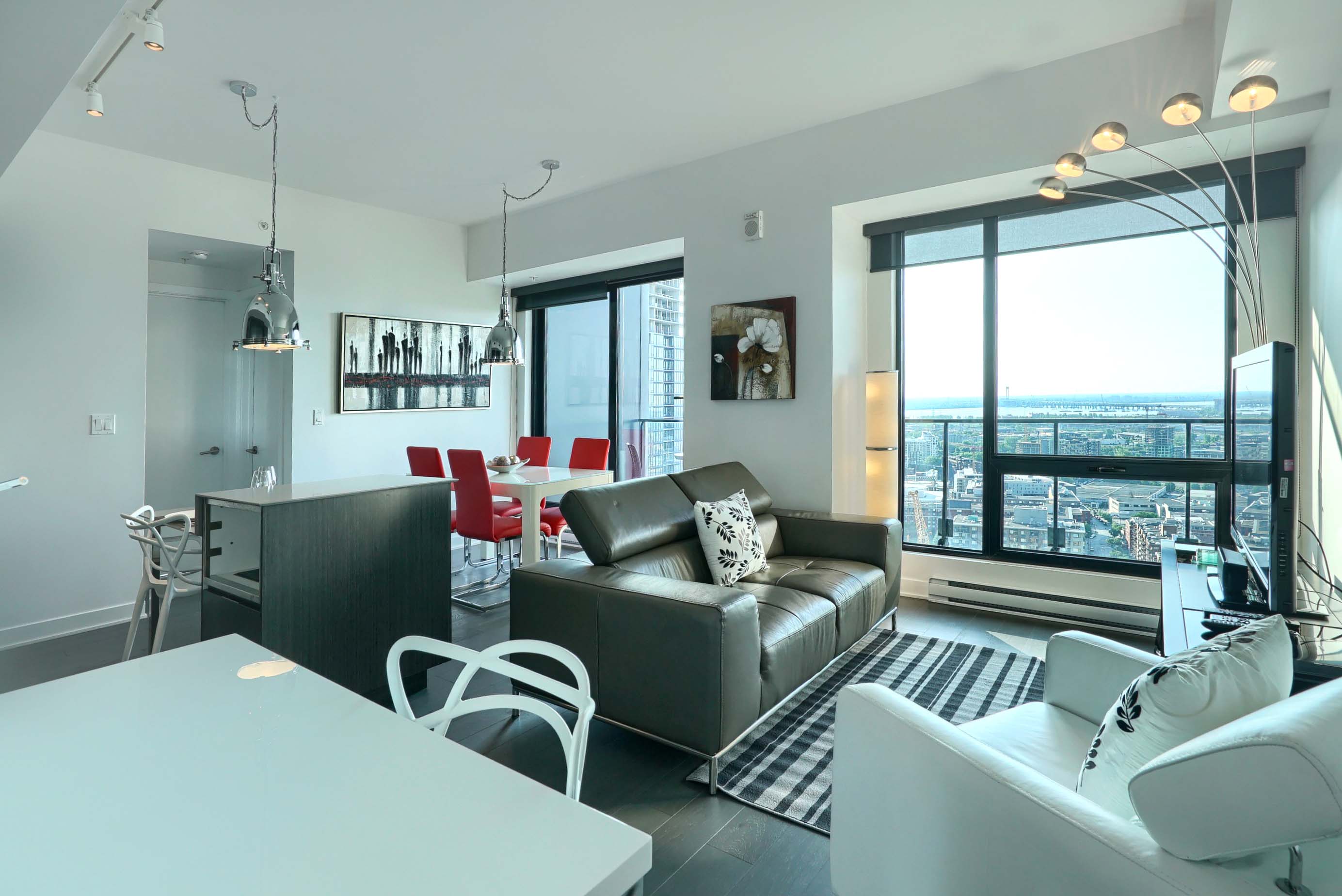 Looking from the office desk into the living room where you can see the modern furnishings, dining table for four and floor-to-ceiling windows in this furnished short term apartment rental in montreal