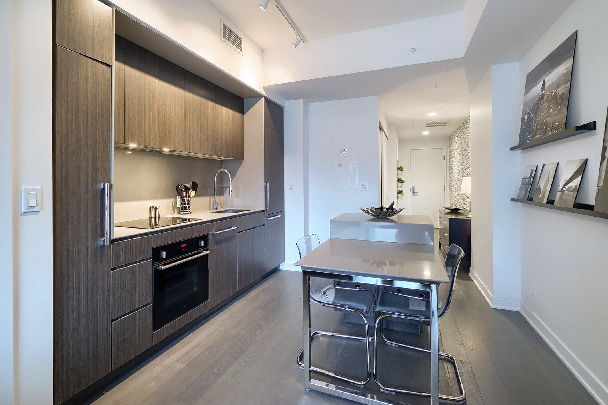 Wide-angle view into the kitchen. Darker gray cabinets against white walls. Spacious and modern kitchen with all the amenities and a nice kitchen island in this furnished corporate suite in Montreal