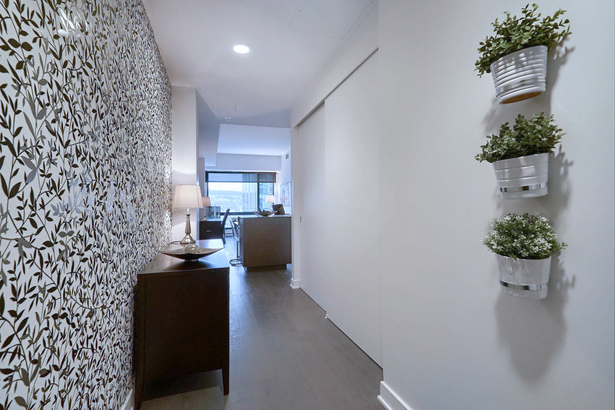 Hall d'entrée de cet appartement entièrement meublé à louer à Montréal. Décorée avec goût, mur floral noir et blanc, belle commode avec vue imprenable sur l'îlot de cuisine