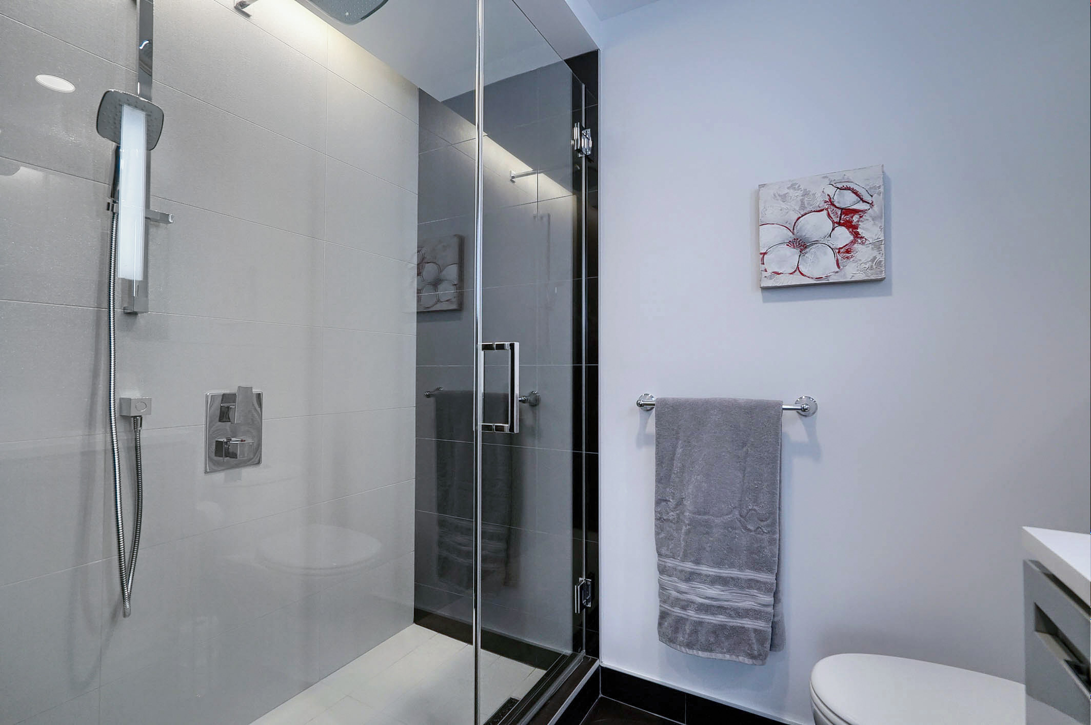 Angled view of the bathroom showing the shower. Glass shower with adjustable shower head in this furnished condo for rent in Montreal.