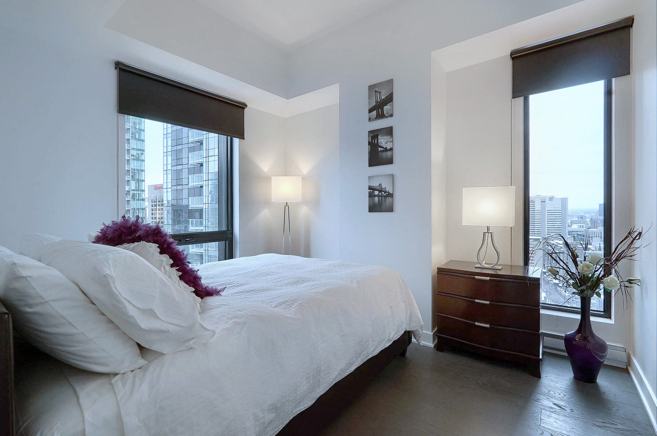 Jetez un coup d'œil dans la chambre à coucher en montrant la literie unique et les deux fenêtres du sol au plafond illuminant votre matinée dans cet appartement meublé de luxe à Montréal