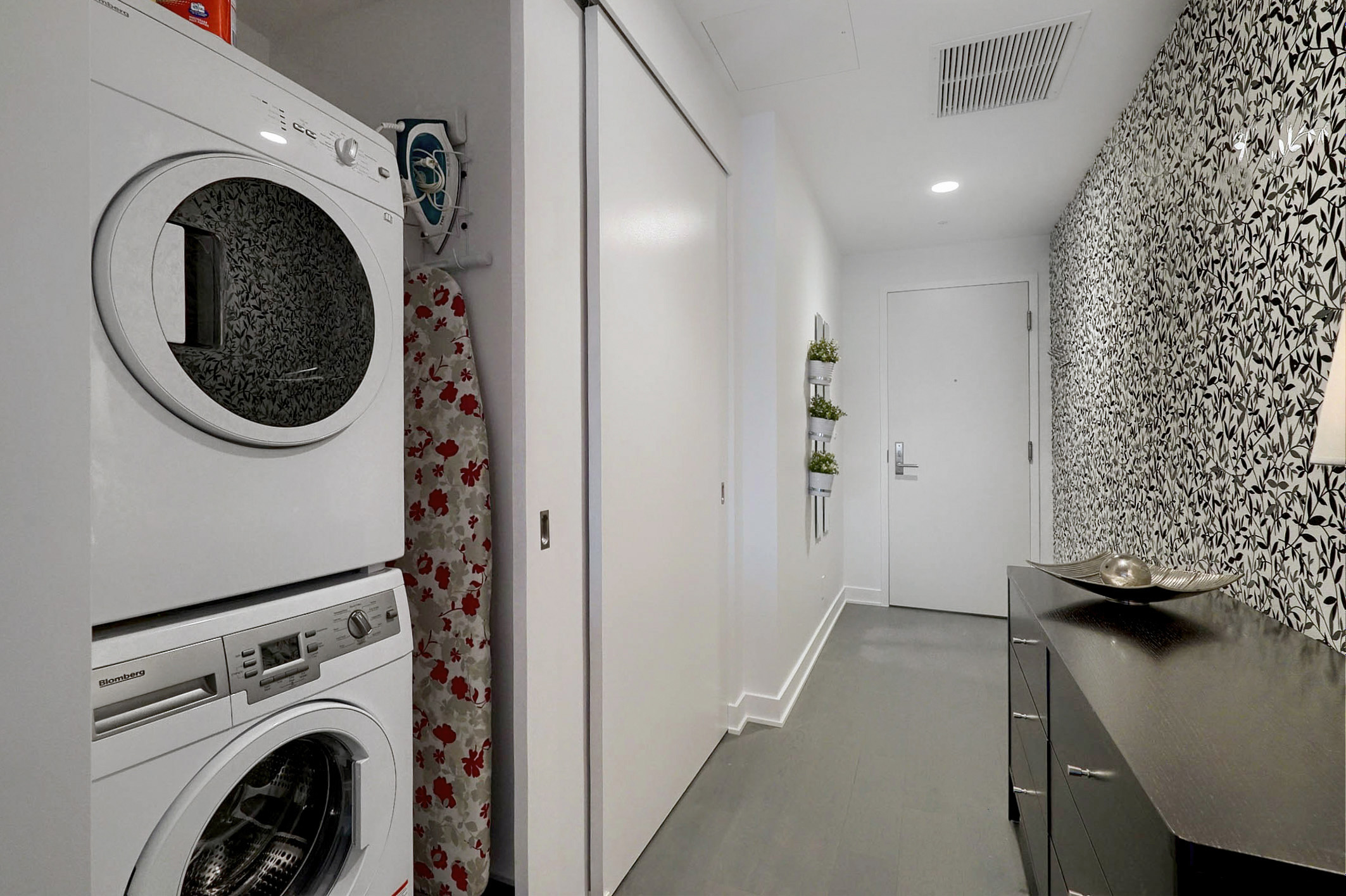 Deep view of the entrance of the apartment showing the sliding door open to see the modern stacked washer & dryer in this luxury furnished corporate housing apartment in Montreal