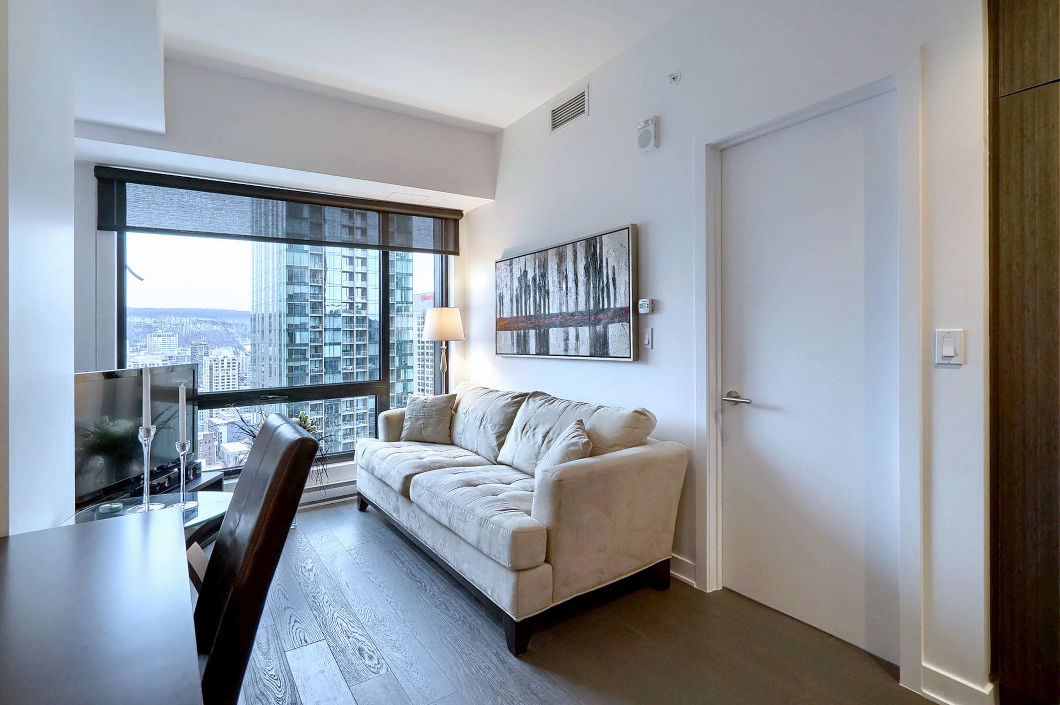 Du bureau au salon, vous pouvez voir le canapé-lit confortable et les baies vitrées de cet appartement meublé à louer à court terme à Montréal