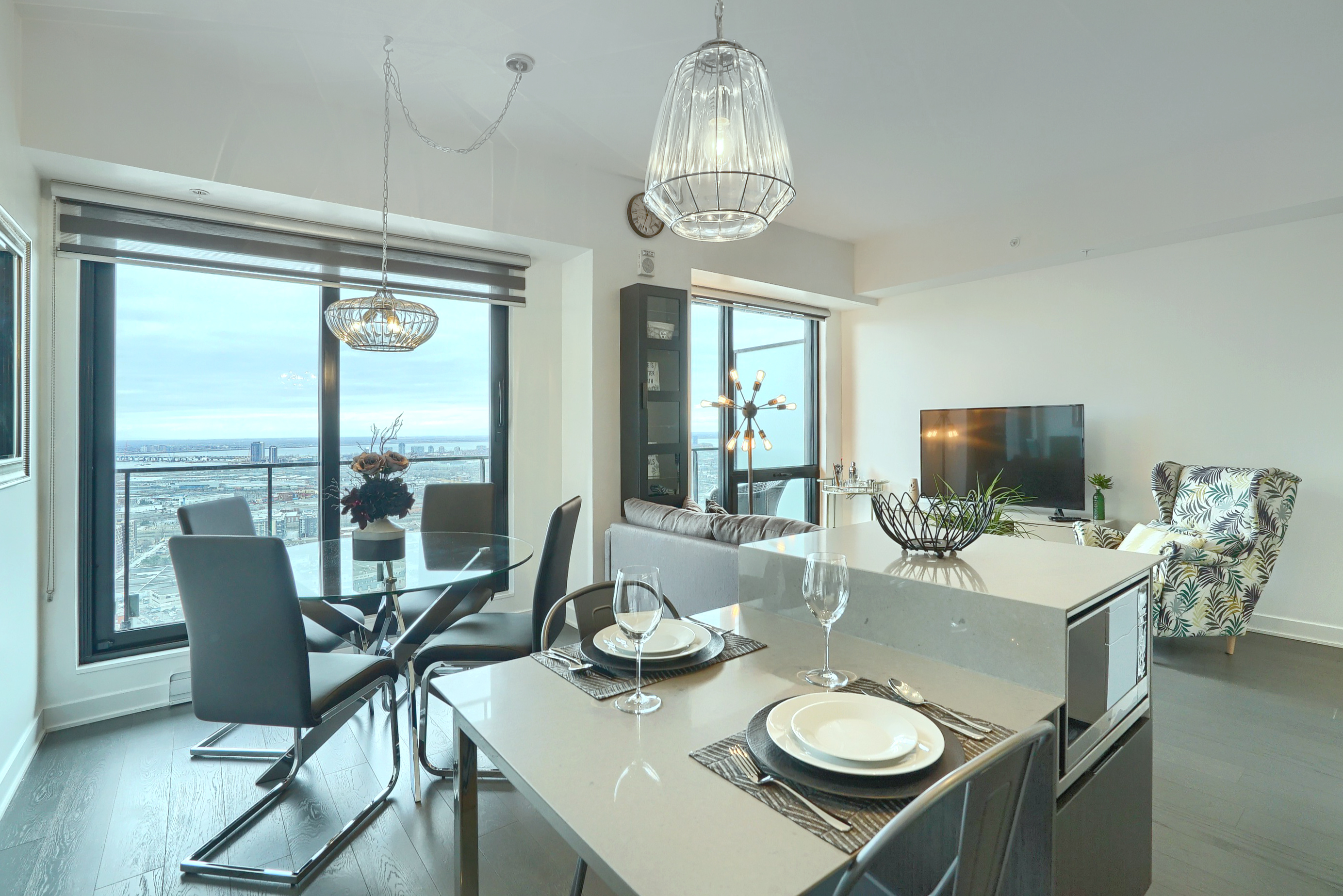 View from the kitchen into the dining and living rooms of this ultra modern luxury furnished rental, short term, in montreal. Seating for four at the glass dining table. Seating for two at the sleek kitchenette. Floor-to-ceiling windows throughout