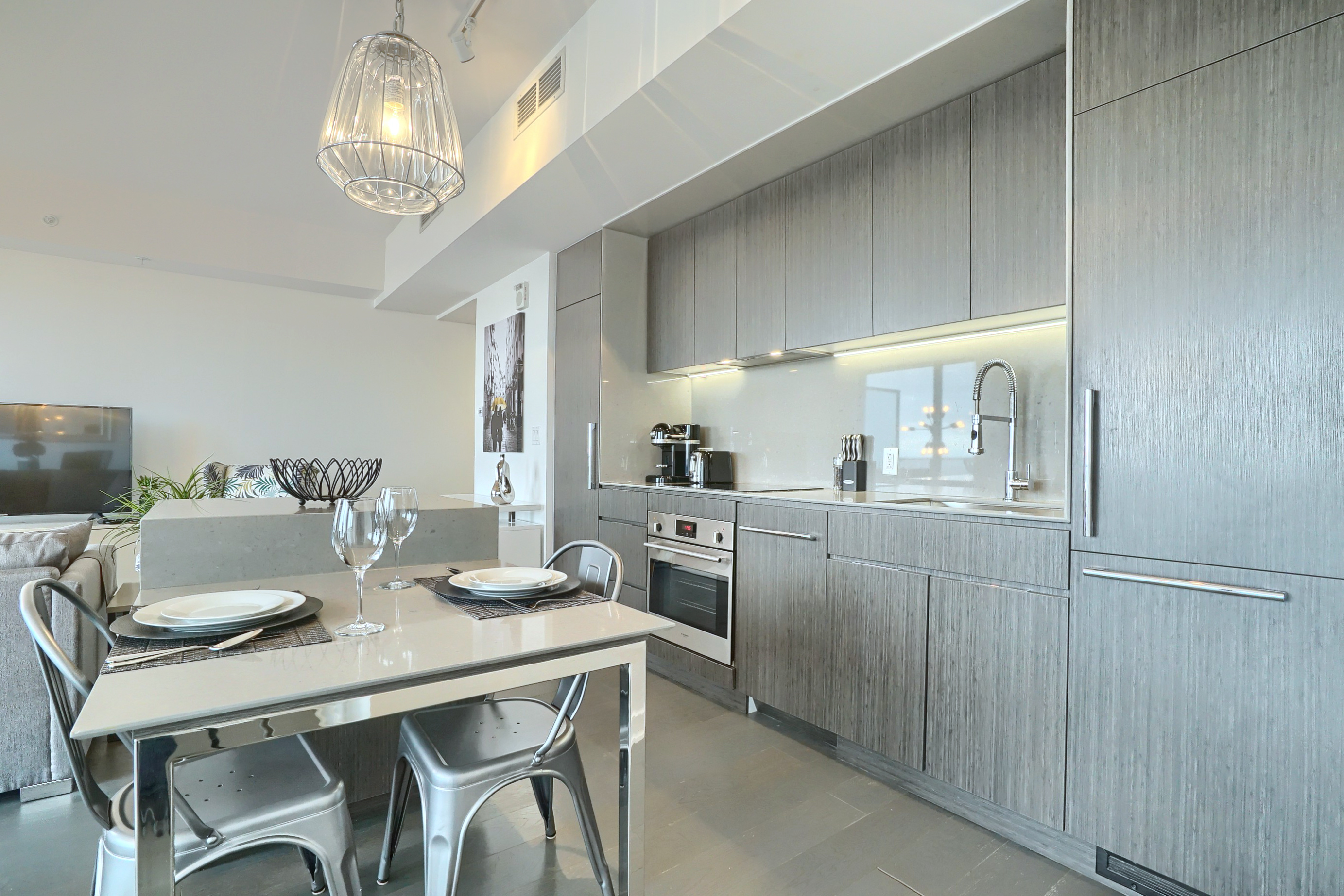 View into the modern, sleek, kitchen. Two seat kitchenette table beautiful decorated with designer placemats, white dishes, tall wine glasses and stainless silverware. Kitchen is bright and spacious - make this furnished condo for rent in montreal perfect