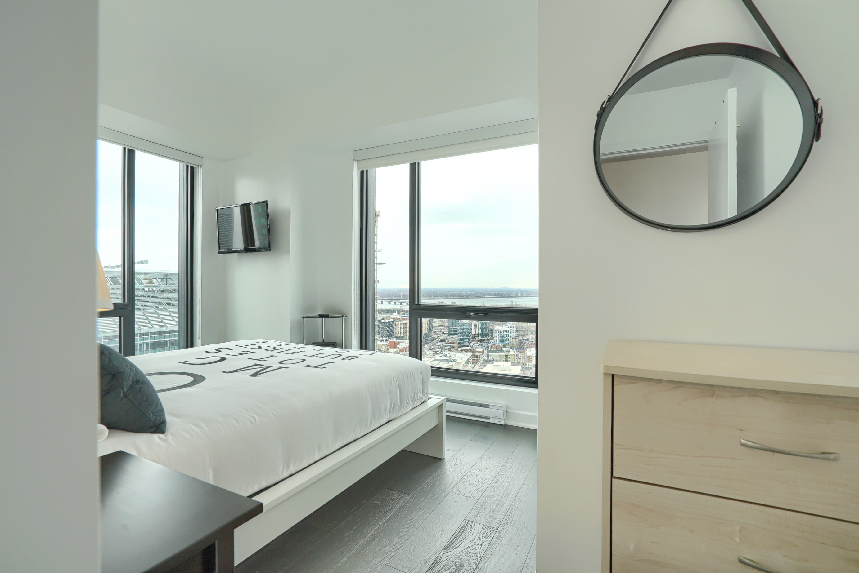 Peek into the bedroom showing the unique bedding - white with gray lettering - and two floor-to-ceiling windows brightening your morning in this furnished executive housing apartment in montreal
