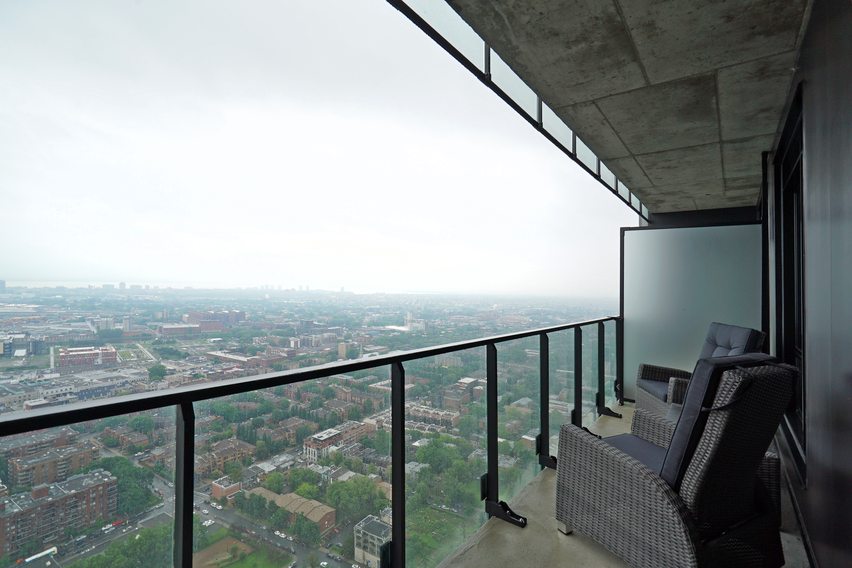 View from the balcony overlooking the magnificent city of montreal. Balcony has a glass railing, dark gray designer outdoor chairs and a glass table. Amazing space from this furnished apartment for rent in montreal