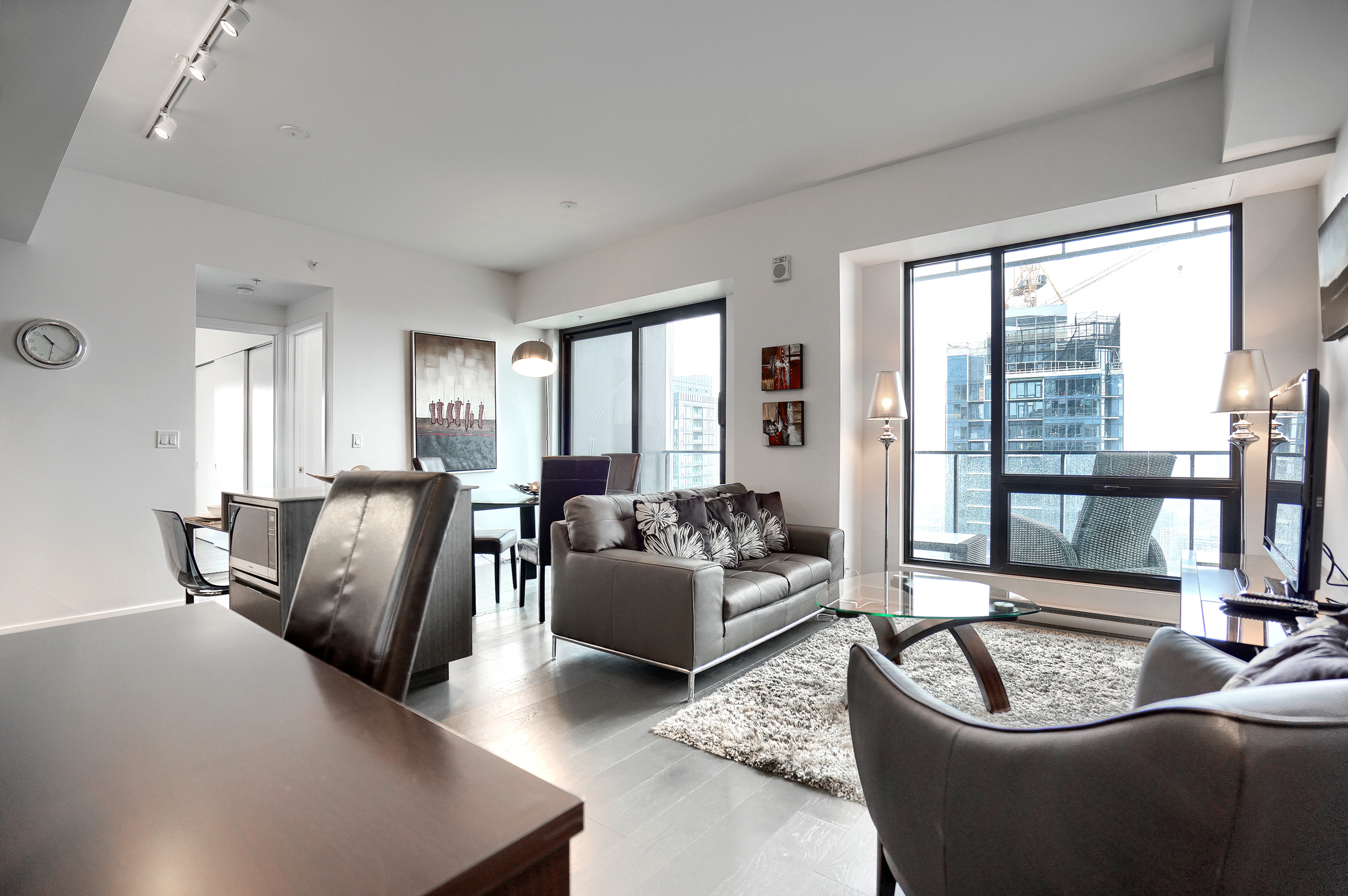 Spacious, bright, beautifully designed living area in this luxury furnished rental in montreal. Two large, floor-to-ceiling windows fills the room with sunlight. Plush leather furnishings, dining area for four, and a study desk and leather chair to match.